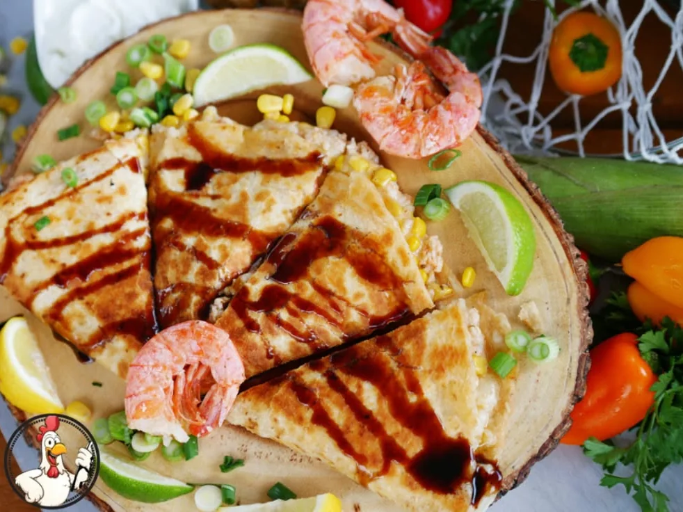 Shrimp and lobster quesadilla cut in wedges on a wooden board, with shrimp and lime